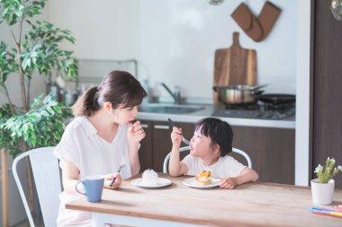 Asyalı anne ve kızı evdeki yemek masasında pasta yiyorlar.
