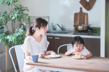 Asyalı anne ve kızı evdeki yemek masasında pasta yiyorlar.