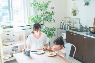 Asyalı anne ve kızı evdeki yemek masasında pasta yiyorlar.