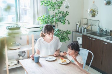 Asyalı anne ve kızı evdeki yemek masasında pasta yiyorlar.