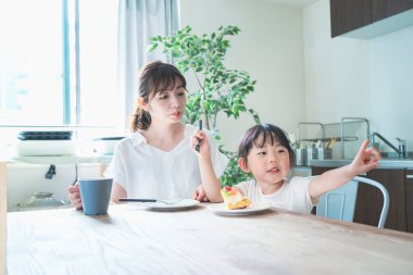 Asyalı anne ve kızı evdeki yemek masasında pasta yiyorlar.