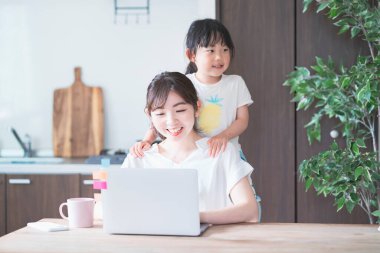 Asyalı bir kadın kızıyla oynarken odasında tele-iş yapıyor.