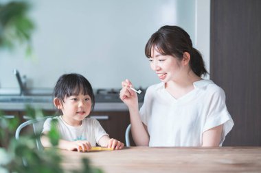 Asyalı genç anne ve kızı odada dişlerini fırçalıyorlar.