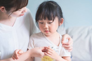 Asyalı bir kız annesini vücut ısısını ölçmeye zorluyor.