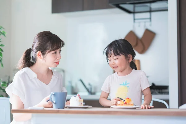 アジアのお母さんと娘は家のダイニングテーブルでケーキを食べる — ストック写真