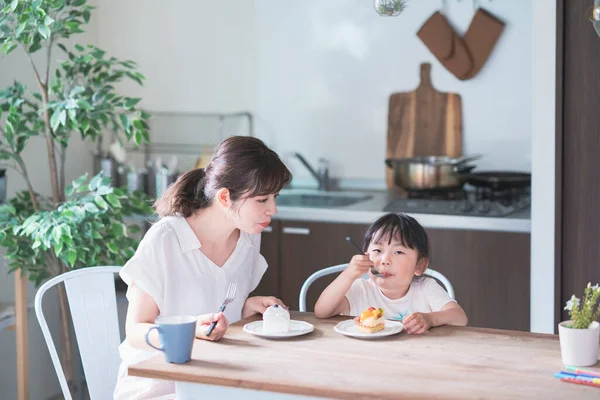 アジアのお母さんと娘は家のダイニングテーブルでケーキを食べる — ストック写真