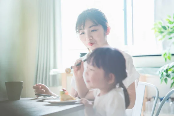 Asian mom and daughter eating cake at dining table at home