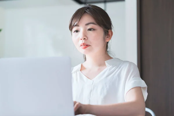 Asian woman doing remote work with laptop at dining table at home