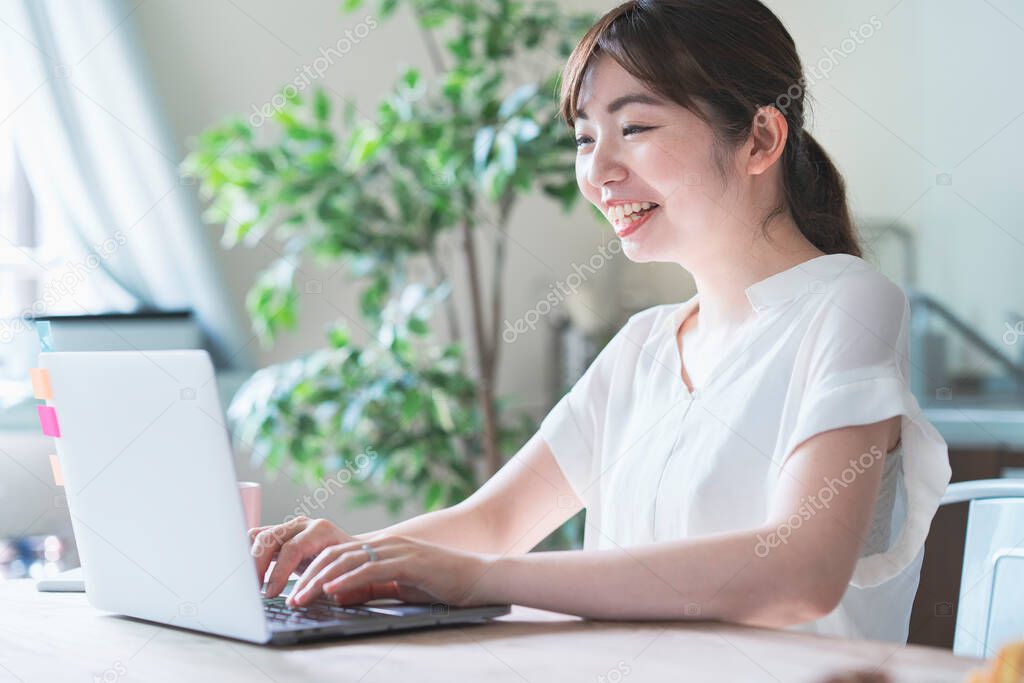 Asian woman doing remote work with laptop at dining table at home