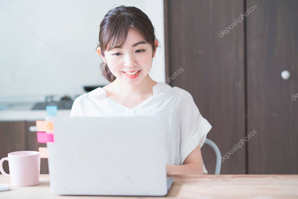 Asian woman doing remote work with laptop at dining table at home