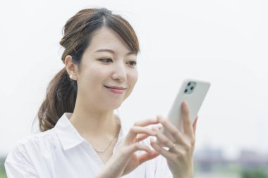 Akıllı telefon ekranına bakarken çalışan Asyalı genç bir kadın.