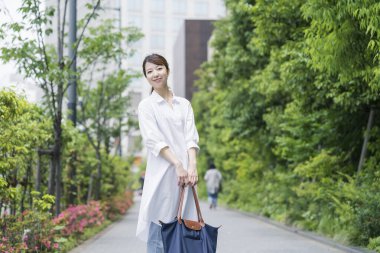 Beyaz gömlekli Asyalı genç ev kadını alışveriş çantasıyla dışarı çıkıyor.