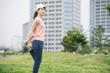 Spor giyinen ve parkta egzersiz yapan Asyalı genç bir kadın.
