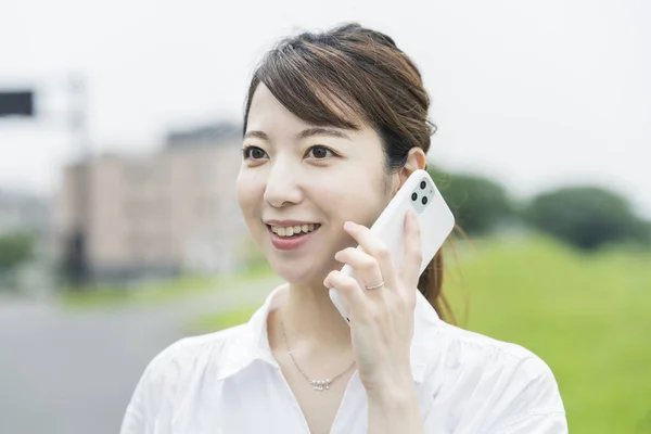 Asyalı Genç Bir Kadın Gülümseyerek Aramak Için Akıllı Telefon Kullanıyor — Stok fotoğraf