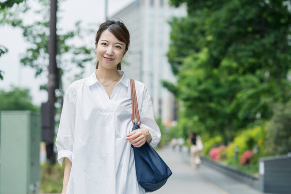 Азиатская молодая домохозяйка в белой рубашке выходит в магазин с сумкой
