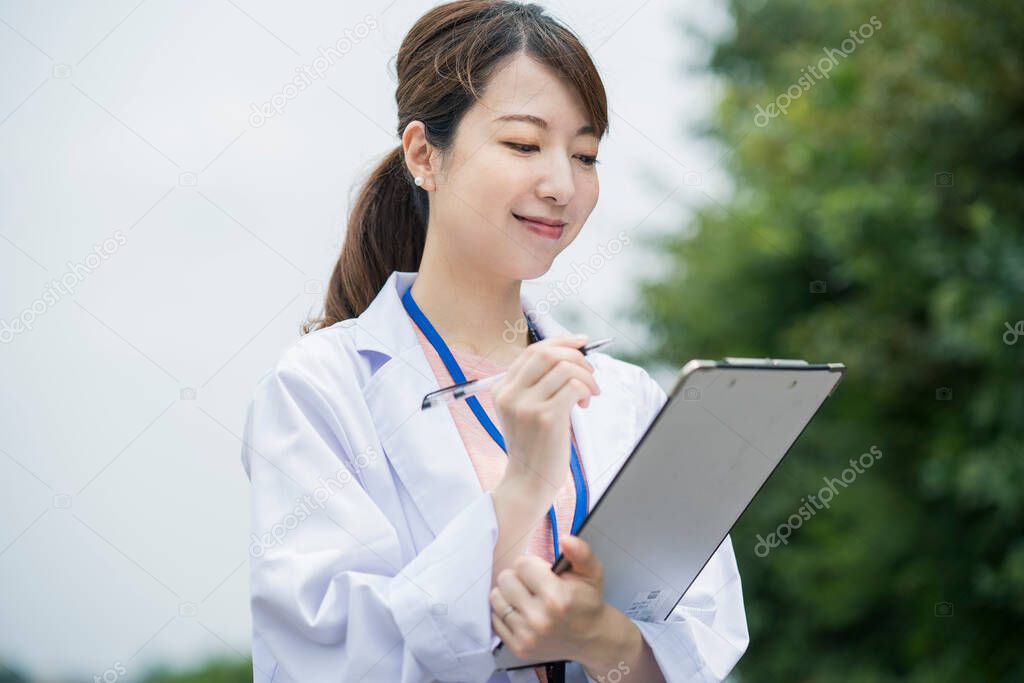 Asian female medical worker in white coat with medical chart and pen