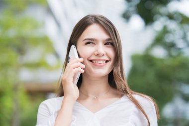 Genç iş kadını dışarıda, akıllı telefonuyla konuşuyor.