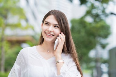 Genç iş kadını dışarıda, akıllı telefonuyla konuşuyor.