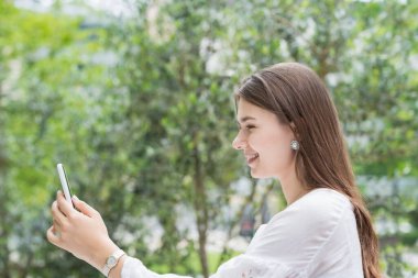 Açık havada akıllı bir telefonun ekranına dokunan ve yöneten bir kadın.