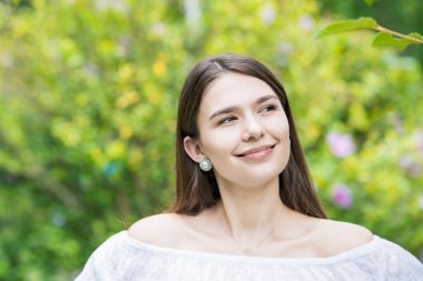 Beyaz omuzlu ve bitkilerle çevrili genç bir kadın.