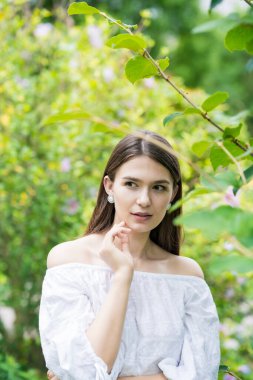 Beyaz omuzlu ve bitkilerle çevrili genç bir kadın.