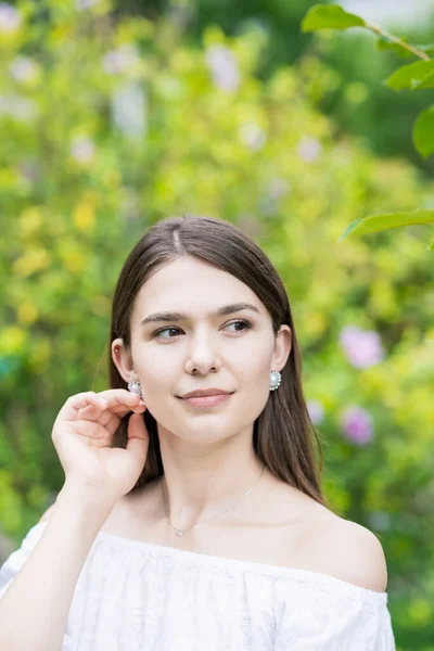 A young woman wearing a white off-shoulder shirt and surrounded by plants