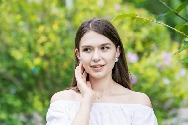 A young woman wearing a white off-shoulder shirt and surrounded by plants