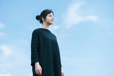 Mavi gökyüzünün altında gevşek bir ifade gösteren genç bir kadın.