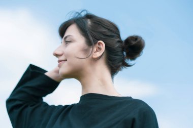 Mavi gökyüzünün altında gevşek bir ifade gösteren genç bir kadın.