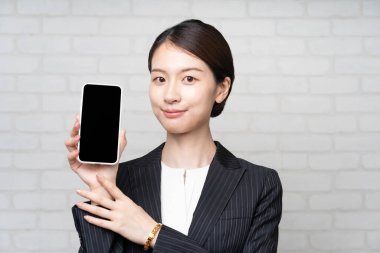 Takım elbiseli Asyalı genç iş kadını akıllı telefon ekranı kullanıyor.