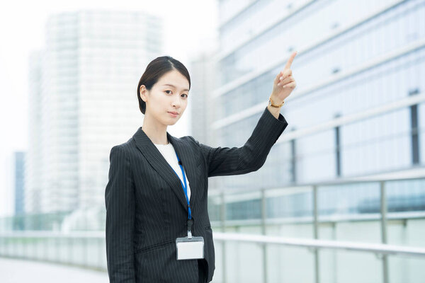 Asian young business woman in a suit pointing diagonally above