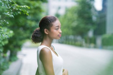 Yeşil bir şehirde kolsuz beyaz gömlekli genç bir iş kadını.