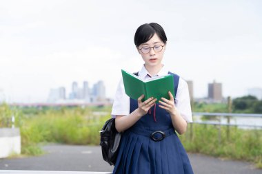 Asyalı liseli kız ciddi bir ifadeyle kitap okuyor.