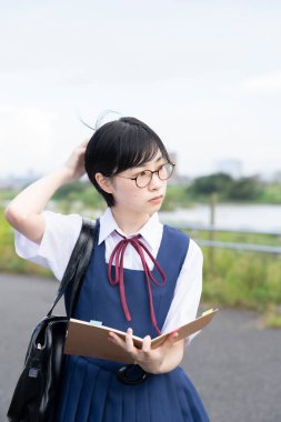 Asyalı kız lise öğrencisi dışarıda ciddi bir ifadeyle ders çalışıyor.