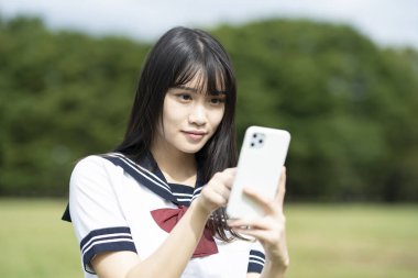 Asyalı lise öğrencisi akıllı telefon ekranına dokunuyor.