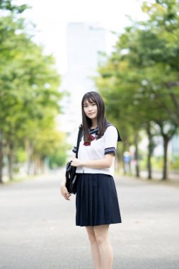 Asyalı kız lise öğrencisi açık havada üniformalı gülümsüyor.