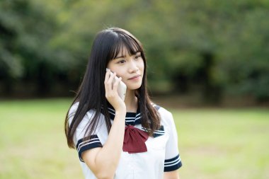 Asyalı lise öğrencisi akıllı telefondan konuşuyor.