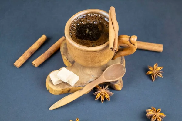 Cup of black coffee and spices on a blue background. In the center of the frame on a wooden stand is a ceramic cup with black coffee. There are muscovado, star anise and cinnamon. offee and spices