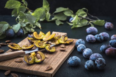 Erikler: dilimlenmiş olgun erikler ve tüm meyveler tahtanın üzerinde, koyu arkaplanda.