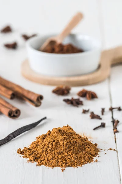 Tarçın, yıldız anason, kakao ve vanilyalı fasulye gibi baharatları beyaz ahşap masada pişirmek. Dikey depo fotoğrafı.