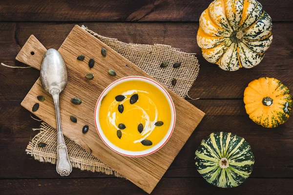 Kremalı balkabağı çorbası ve kabak tohumları koyu kahverengi ahşap arka planda, küçük balkabakları, kaşık ve çekirdekler ile süslenmiş,.