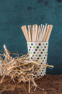 Bambu kabında pipet içen doğal pipet ve eski bir ahşap kirişin üzerinde bir demet saman, yeşil arka plan. Sürdürülebilirlik kavramı, plastik yok. Kopyalama alanı ile dikey.
