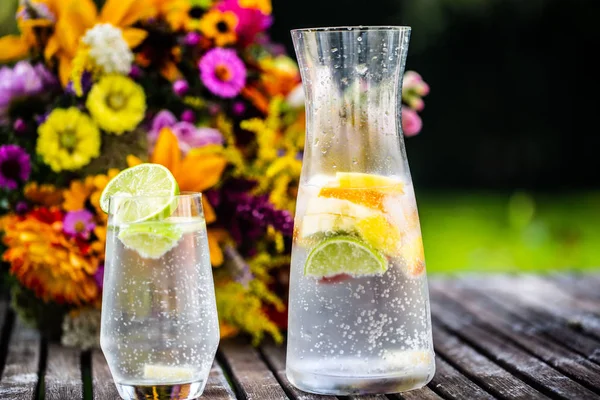 Wasser mit frischen Früchten in Karaffe, grüner Hintergrund, Garten — Stockfoto