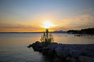 Bardolino 'da gün batımı Garda Gölü' nde, arkasında dağlar var.