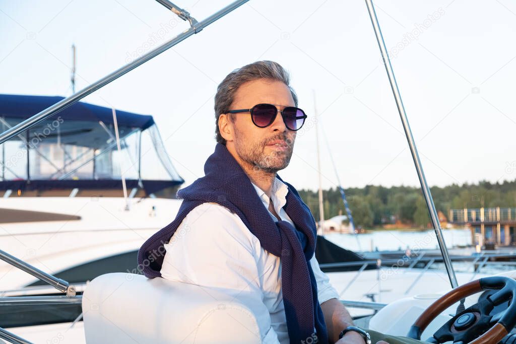 Handsome man wearing sunglasses on the yacht. Portrait of smiling man on sailing boat at sunset in marina.