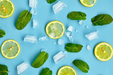 Mavi arka planda kesilmiş turunçgil meyveli kompozisyon. Limon dilimleri, nane yaprakları ve buz küpleriyle yaratıcı bir yaz kompozisyonu. Limonata içeceği konsepti. Üst görünüm.