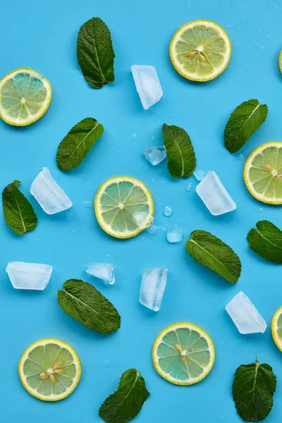 Composition with cut citrus fruits on blue background. Creative summer background composition with lemon slices, leaves mint and ice cubes. Minimal top down lemonade drink concept.Top view