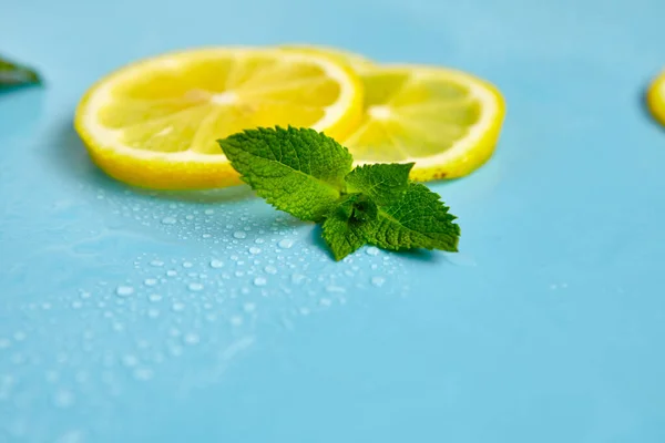 Composition with cut citrus fruits on blue background. Creative summer background composition with lemon slices, leaves mint and ice cubes. Minimal top down lemonade drink concept. Top view