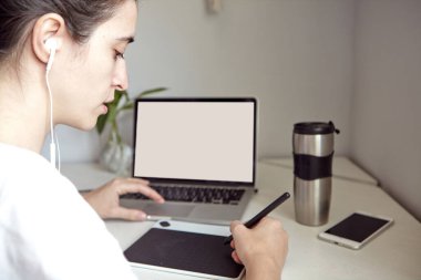 Kız evde grafik tableti ve dizüstü bilgisayar üzerinde çalışıyor. Evde bir bilgisayarda çalışan genç bir kadın. Mesafe çalışması kavramı