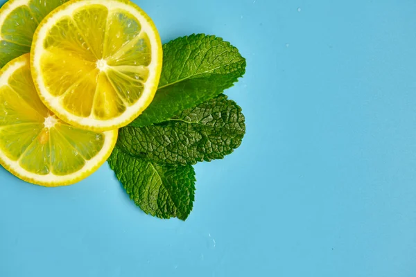 Composition with cut citrus fruits on blue background. Creative summer background composition with lemon slices, leaves mint and ice cubes. Minimal top down lemonade drink concept. Top view